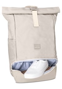 Beige roll-top backpack made of smooth material, featuring a zipper compartment revealing white sneakers. Includes a label logo and side pocket.