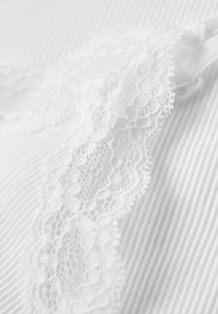 Tela blanca con rayas verticales, que presenta un delicado borde de encaje a lo largo del borde, destacando patrones intrincados y una textura suave.