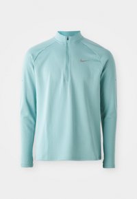 Jasnoniebieski longsleeve z zamkiem błyskawicznym przy kołnierzu, teksturowana tkanina oraz szare logo Nike na piersi. Posiada rękawy raglanowe.