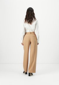 Beige, magas derekú nadrág egyenes szárú kialakítással, sima anyagból készült. Hátul zsebekkel és öves derékrésszel rendelkezik, fehér inggel párosítva.