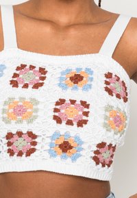 Top corto de crochet blanco con patrones florales coloridos en rosa, azul, verde y marrón. Tirantes ajustables con un acabado texturizado.