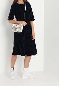 Abito navy con texture, maniche corte e gonna a strati, abbinato a una borsa a tracolla con motivo floreale e stivali combat bianchi.
