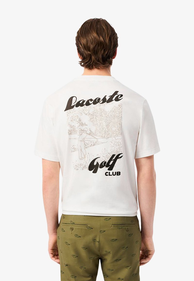 Camiseta blanca de algodón con un diseño gráfico en la parte de atrás que presenta el texto "Lacoste Golf Club" y una ilustración de un golfista en un entorno de parque.