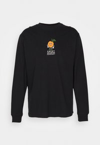 Chemise noire à manches longues avec un petit motif brodé d’un dessin animé orange en colère et le texte « ANGRY ORANGE KAOTIKO SOCIETY » sur la poitrine.