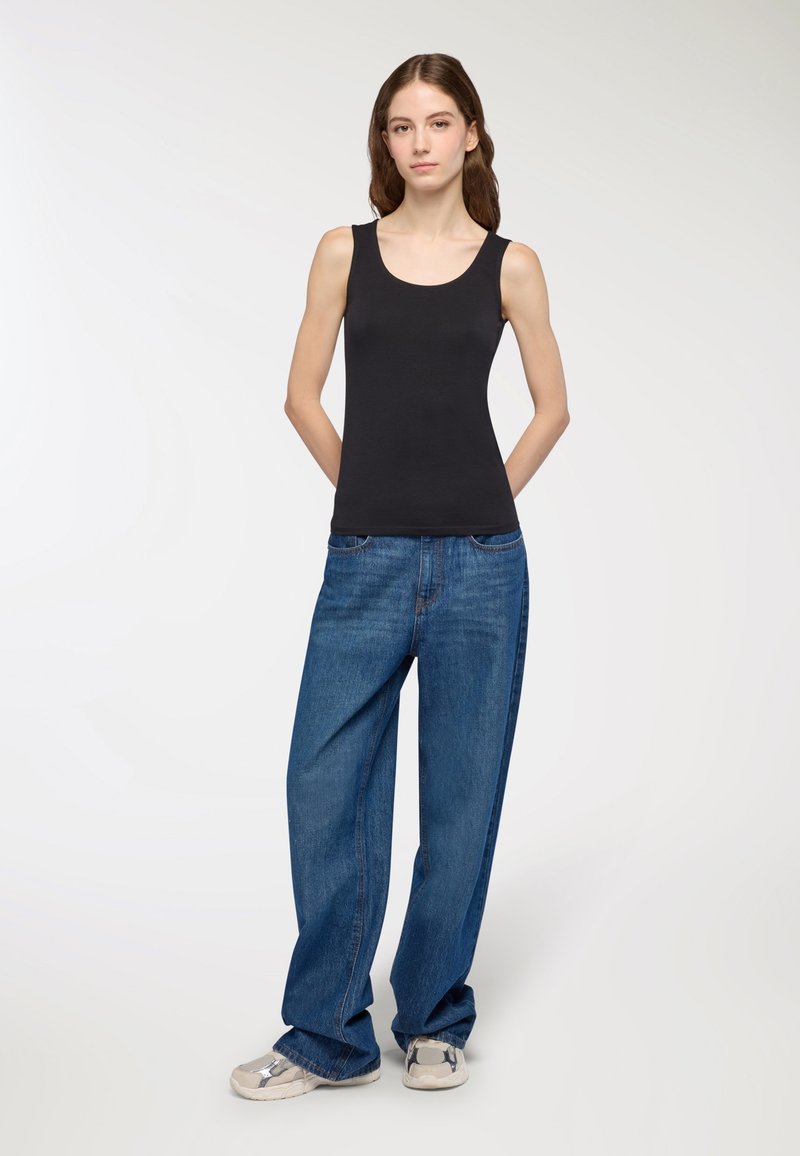 Canotta nera con scollatura a girocollo, abbinata a jeans in denim blu a vestibilità ampia. La canotta è aderente, mentre i jeans hanno un taglio rilassato.