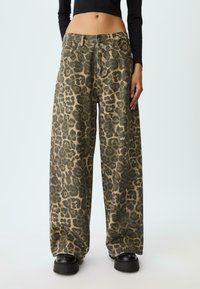 Pantaloni a gamba larga con stampa leopardata verde e marrone indossati con scarpe platform nere e un top cropped a maniche lunghe nere.