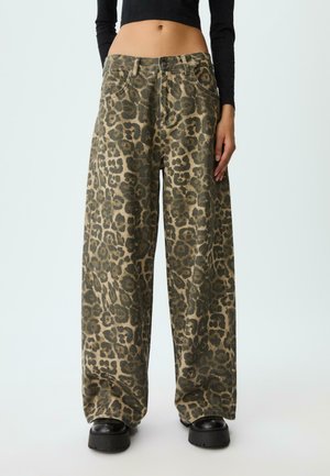  Wijde broek met groen en bruin luipaardprint, gedragen met zwarte platform schoenen en een cropped zwart langemouwen top.