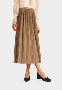 Gonna beige plissettata con una cintura liscia, abbinata a una blusa crema. Ballerine nere con un piccolo dettaglio a fibbia.