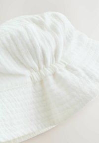 White cotton bucket hat with gathered design, textured fabric, and a soft, flexible brim. Seam details visible along the edges.