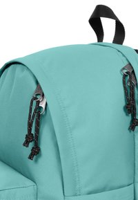 Turkos ryggsäck med svart hårdvara, med en överdel som flik och dragsko, tillverkad av hållbart tyg med en slät yta.