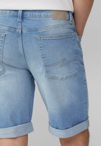 Shorts en denim bleu clair avec ourlets roulés, présentant un design simple, des poches arrière et un léger détail de couture sur la poche droite.