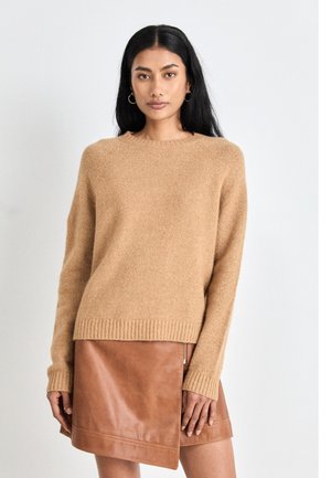 Beige gestrickter Pullover mit rundem Ausschnitt und geripptem Saum, kombiniert mit einem kastanienbraunen Lederwickelrock mit seitlichem Reißverschluss. Glatte Textur, lässige Passform.