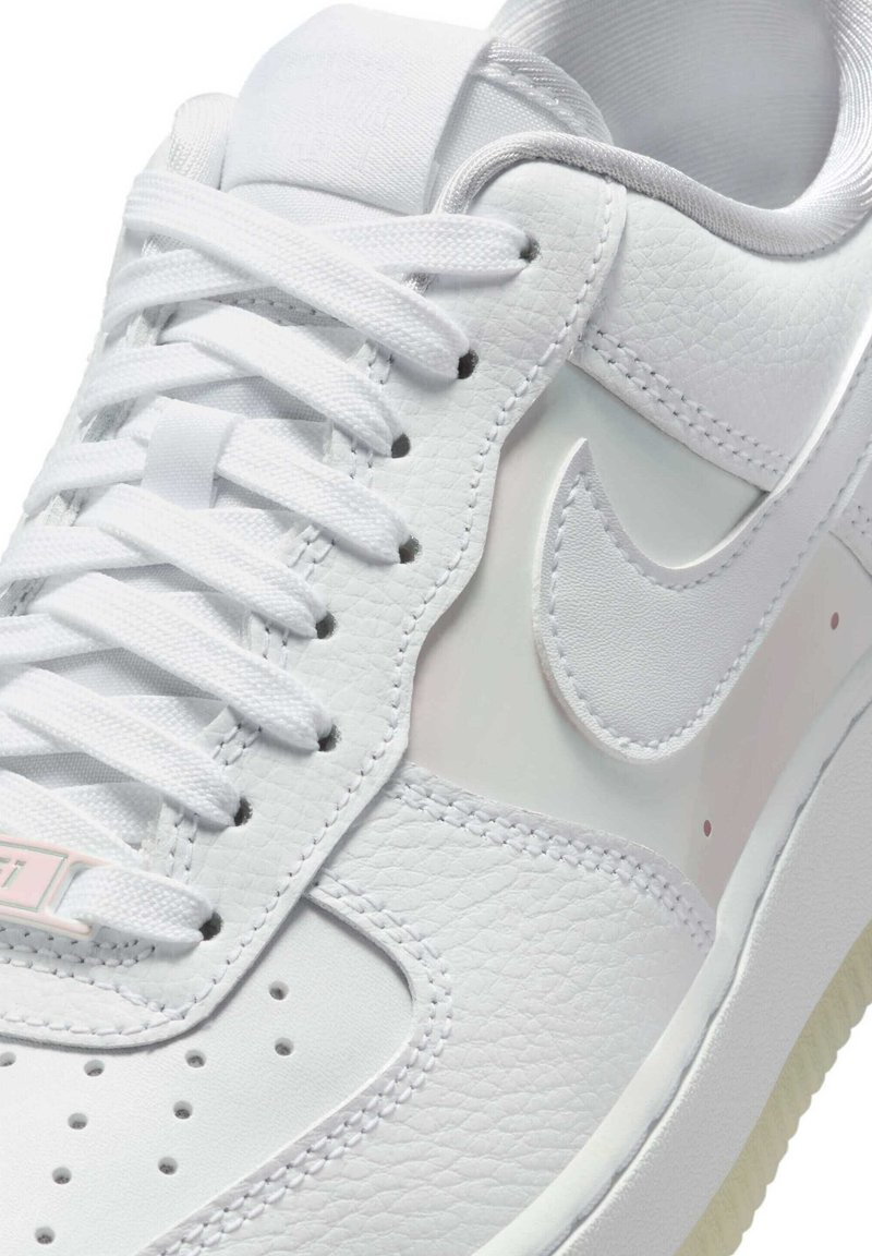 Witte leren sneaker met een gladde textuur, platte veters, perforaties op de neus en een glanzend accent aan de zijkant met een logo.