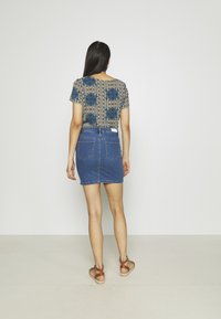 Haut à manches courtes à motif floral bleu, associé à une jupe mini en jean ajustée. Des sandales marron à lanières complètent le look.