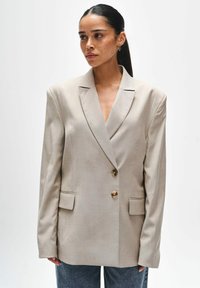 Beige oversized blazer gemaakt van textuurstof, met notch-lapels, twee knopen aan de voorkant en klepzakken aan de zijkanten.
