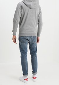 Grå hættetrøje, blå denim jeans og hvide sneakers med røde accenter. Casual pasform med ribbede manchetter og kant.