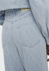  Lichtblauwe denim jeans met een subtiel geometrisch patroon, voorzien van twee achterzakken en een gestructureerde afwerking.