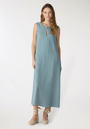 Donna che indossa un abito lungo azzurro chiaro senza maniche con spacco frontale sullo scollo, abbinato a sandali espadrillas beige con zeppa e lacci alla caviglia.