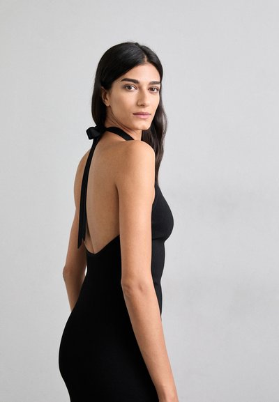 Must mustriga kleit sügava selja lõikega ja kaelas kinni seotud paelaga. Sile kangas, keha lähedane siluett ja minimalistik disain.