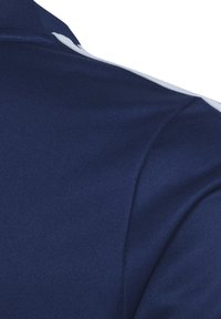 Camicia blu scuro con un tessuto testurizzato. Presenta una striscia bianca decorativa sulla spalla. Design con colletto alto e maniche corte.