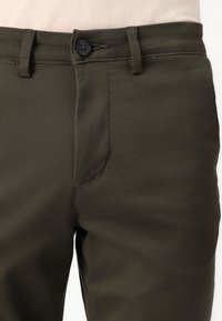 Tmavě zelené kalhoty z bavlněné směsi mají zapínání na knoflík, poutka na opasek, plochý přední díl s hladkou strukturou a boční kapsu.