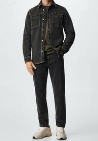 Chaqueta de mezclilla oscura con dos bolsillos en el pecho, combinada con jeans oscuros y zapatillas beige. La tela tiene una textura resistente.
