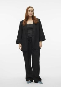 Černý lněný kimono kabát se širokými rukávy, v kombinaci s černým tílkem a volnými černými kalhotami. Měkká textura, minimalistický design, modré špičaté baleríny.