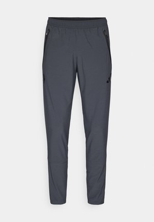 Grå træningsbukser med elastisk talje, lynlåslommer i siden og et logo detaljeret på venstre lår. Fremstillet af letvægtsstof.