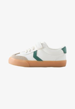 Biały niski sneaker z zielonym detalem w kształcie jodełki, beżowym zamszowym noskiem, paskiem na rzep oraz jasnobrązową gumową podeszwą.