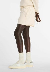 Beige drawstring shorts with side pockets, paired with cream socks and off-white sneakers featuring grey accents and textured soles.