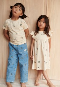 Light-colored cotton t-shirt with floral print, paired with blue denim pants. Child in a beige dress with ruffled sleeves and similar floral design.