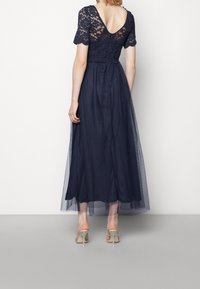 Marinblå golvlång klänning med spetsliv, korta ärmar och en full tullekjol. Öppen ryggdesign med en knappknäppning.