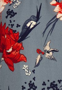 Tessuto a motivi floreali con fiori rossi e bianchi, un uccello blu e vari fiori piccoli su uno sfondo grigio testurizzato.