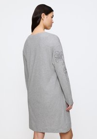 Grå bomullsklänning med långa ärmar och en blommig konturdesign på vänster arm. Enkel, rak skärning som når till mitten av låret.