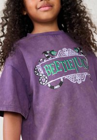 Lila bomull t-shirt med en svart och grön "Beetlejuice" grafik med ormslipat accent och en sliten finish.