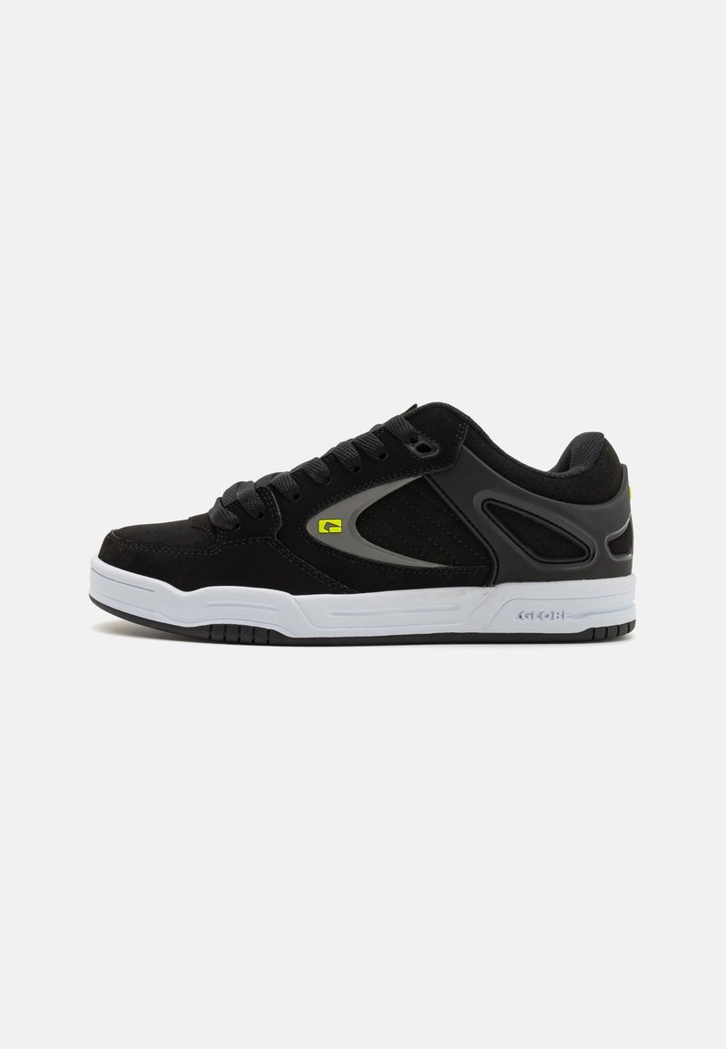 Sneaker nera con una combinazione di materiali scamosciati e sintetici, suola bianca, design con lacci e accenti di logo giallo.