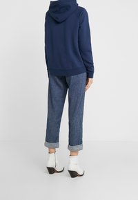 Felpa navy con tasca a marsupio, abbinata a pantaloni di denim azzurri a risvolto e stivaletti bianchi con tacco.