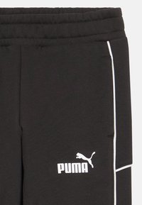 Zwarte sweatpants van zachte stof, met een wit logo en accenten in de trim. Elastische tailleband en zijzakken zijn zichtbaar.