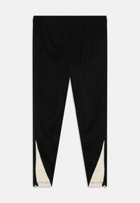 Pantalon de sport noir avec une taille élastique, présentant des accents crème au niveau des chevilles et des zips pour ajustement. Texture lisse.