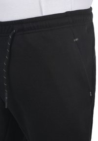 Sorte joggebukser med elastisk talje og snøring, med sidelommer og et lille logo mærke. Blød stoftekstur.