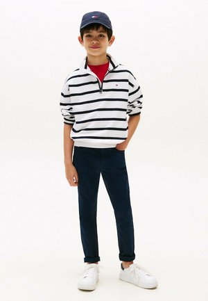 Pull en rayures blanches et marines, couche de base rouge, pantalon marine, baskets blanches et casquette marine avec logo. Coupe décontractée, style casual.