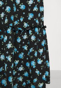 Schwarzer Stoff mit einem blauen Blumenmuster, verziert mit gerüschten Akzenten am Saum. Leicht und strukturiert mit sichtbaren Schichten und floralen Details.
