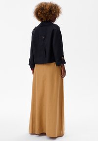 Czarna krótka kurtka z dużym kołnierzem, rękawami na guziki i naszywaną kieszenią, w zestawieniu z długą, jasnobrązową spódnicą wykonaną z strukturalnej tkaniny.