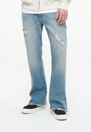 Lichtblauwe denim jeans met een ontspannen pasvorm, voorzien van gescheurde details en rafelige zomen. Draagt met zwarte sneakers.