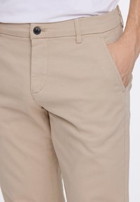 Beige katoenen broek met een slim fit, voorzien van zijzakken, een frontale knoopsluiting en subtiele stikdetails.