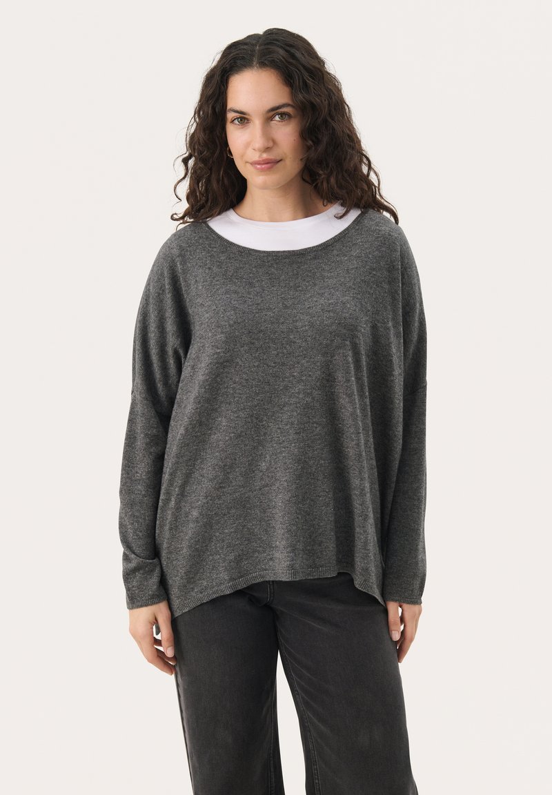 Dark grey knitted sweater with a loose fit, wide neckline, and long sleeves, paired with black jeans. Soft texture, minimal design.
