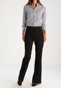 Schwarze, ausgestellte Hose kombiniert mit einem navy- und weiß gestreiften Hemd mit Knöpfen. Das Hemd hat einen Kragen und lange Ärmel mit Knopfabschlüssen.