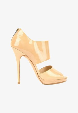 Chaussure à talon haut en cuir verni beige avec bout ouvert, large bride au milieu du pied, talon aiguille haut et fermeture éclair arrière.