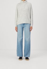 Light grey ribbed sweater with a zip collar, paired with wide-leg light blue jeans. Model wears black shoes with a gum sole.