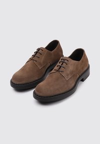 Zapatos de ante marrón con punta redondeada, suela de goma negra y diseño clásico de cordones. Textura suave y detalles de costura mínimos.